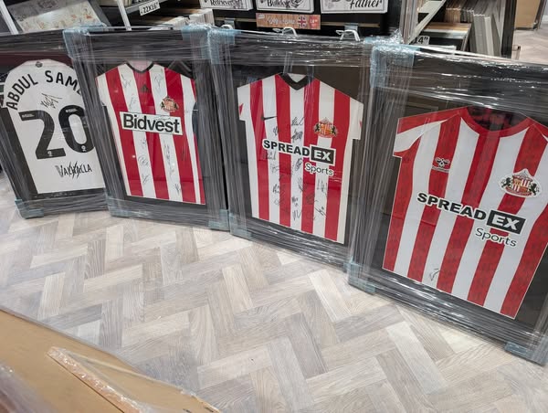 Framed football shirts with visible branding on a herringbone floor.